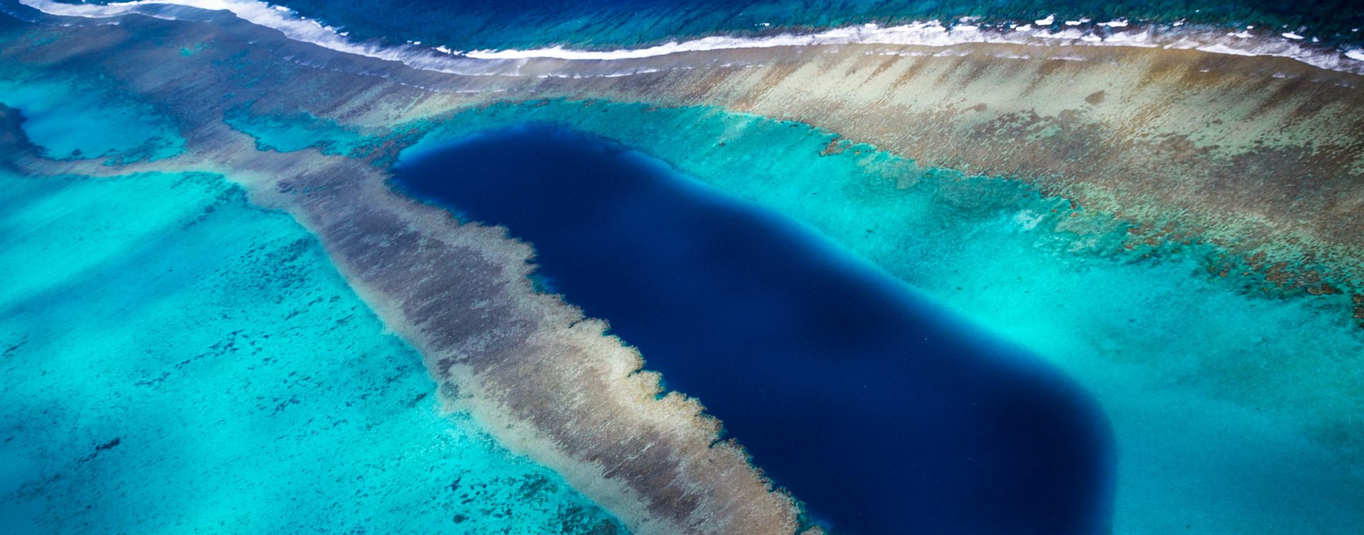 A deep blue hole in a turquoise reef in New Caledonia, seen from the air