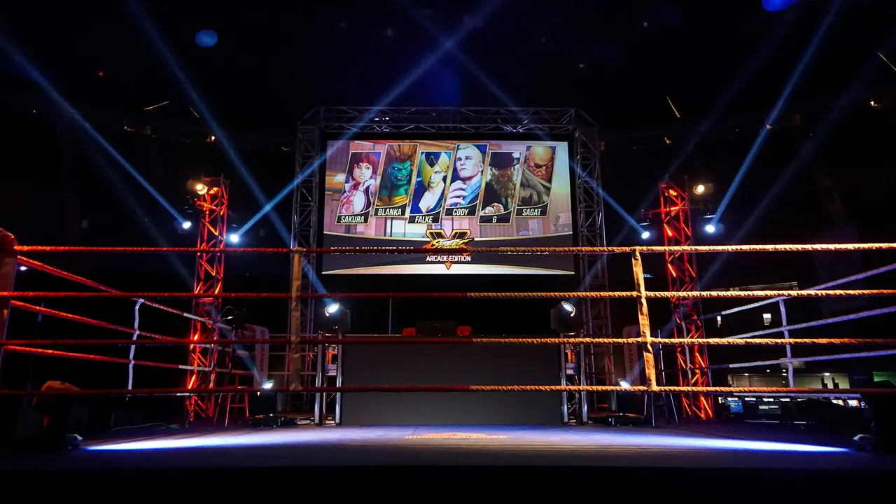 A boxing-ring stage under spotlights with a big screen showing Street Fighter characters